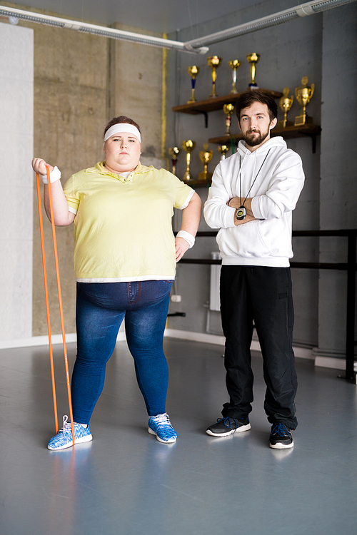 Full length portrait of confident overweight woman posing with personal fitness coach during workout