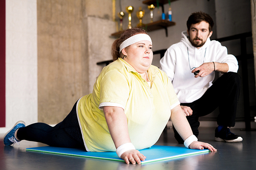 Portrait of  overweight young woman working out on floor with personal fitness instructor in health club, copy space