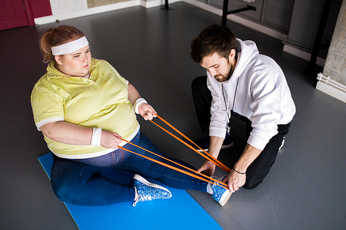 High angle portrait of  overweight woman stretching on floor with personal fitness instructor in health club, copy space