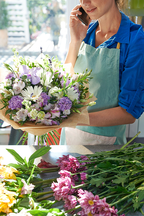 Crop view of unrecognizable florist speaking by phone while arranging flowers in shop