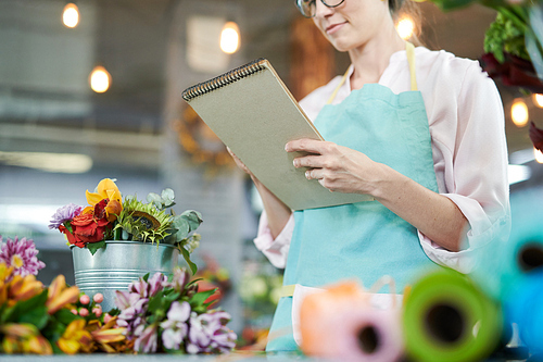 Mid section portrait of young woman wearing apron holding notepad while counting finances  in flower shop