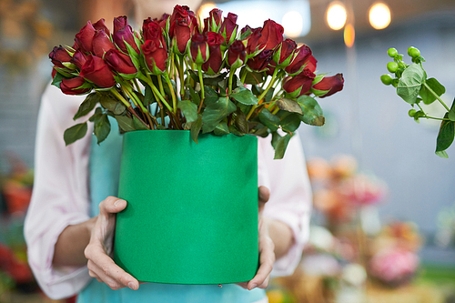 Closeup of unrecognizable female florist holding vase with beautiful red roses while working in flower shop, copy space
