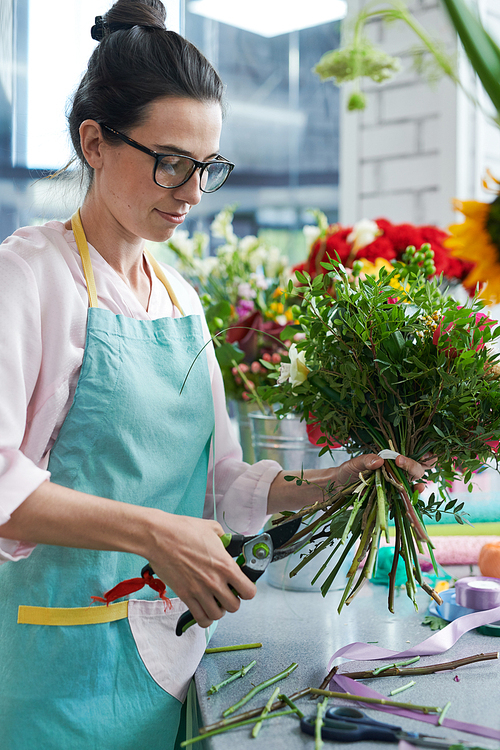Side view portrait of female florist wearing apron arranging bouquets in flower shop and smiling