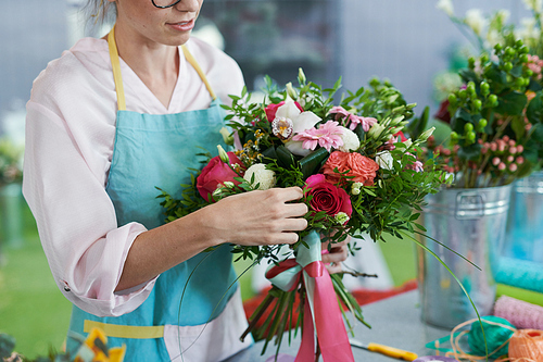 Mid-section portrait of female florist wearing apron arranging beautiful bouquets in flower shop, copy space
