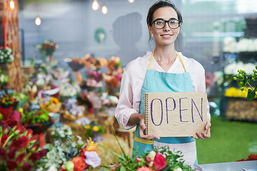 Portrait of modern young woman holding handwritten OPEN sign and smiling at camera while working in small flower shop, copy space