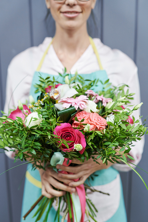 Crop view of closeup young florist in work uniform holding beautiful rose bouquet