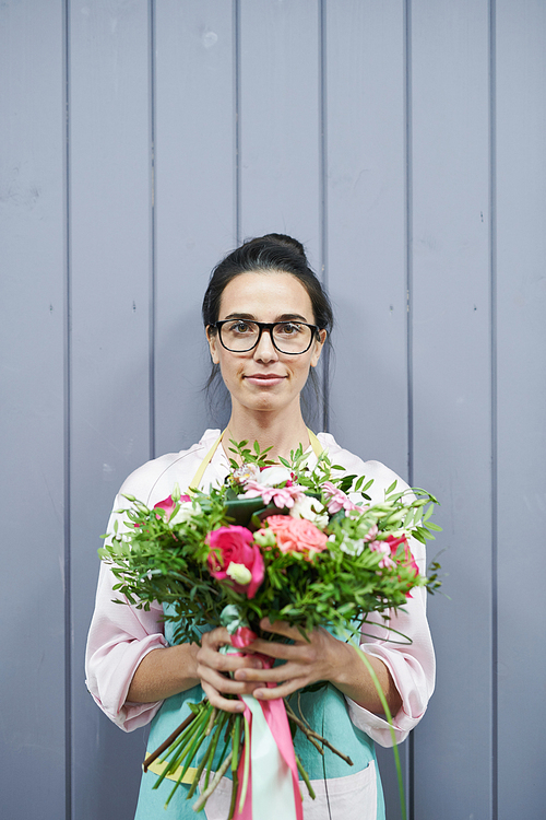 Waist up portrait of modern female florist holding beautiful bouquet and  posing by grey wooden wall, copy space