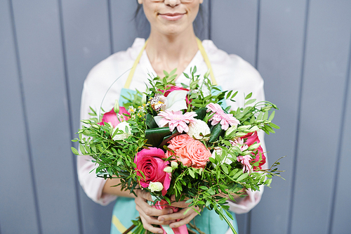 Mid section portrait of  female florist holding beautiful rose bouquet  posing by grey wooden wall, copy space