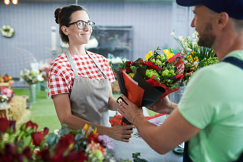 Waist up portrait  smiling young woman giving bouquet to delivery guy in small flower shop, copy space