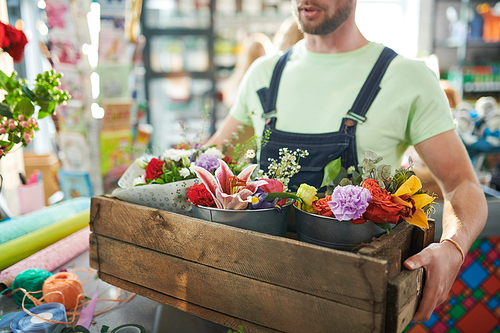 Mid section portrait of unrecognizable worker holding wooden box with flowers while bringing supply to flower shop, copy space