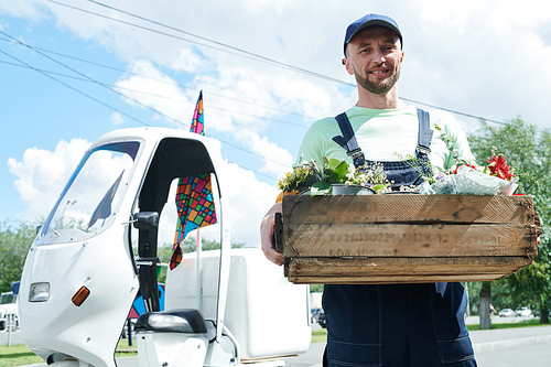 Portrait of handsome worker holding box with flowers, copy space