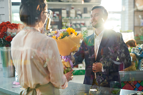 Portrait of handsome man buying beautiful bouquet and smiling happily while taking flowers in sunlit shop, copy space