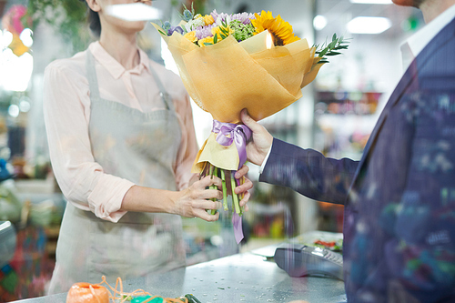 Mid section portrait of  female shopkeeper handing bouquet to handsome gentleman buying flowers for date or celebration, copy space