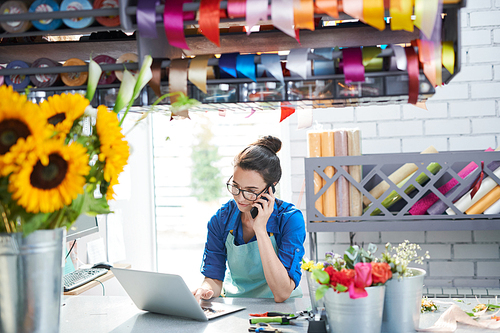 Portrait of young female businesswoman managing flower shop and speaking by phone, copy space