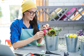 Portrait of smiling contemporary woman arranging flower compositions and using laptop in shop, copy space