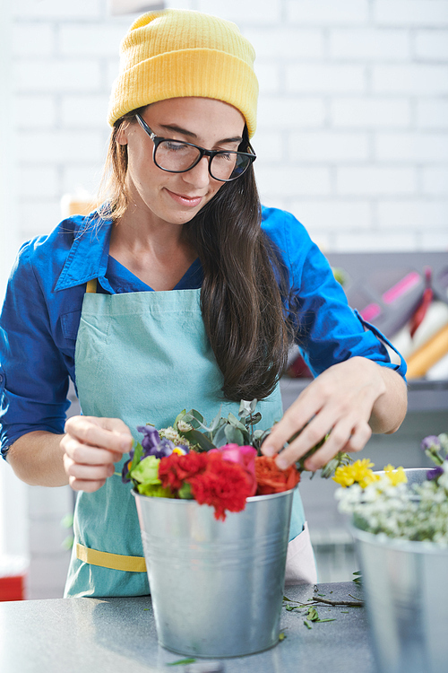 Portrait of contemporary young woman lovingly arranging flower compositions while working in shop