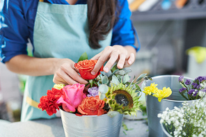 Closeup of female hands arranging beautiful flower compositions with roses on display in shop, copy space