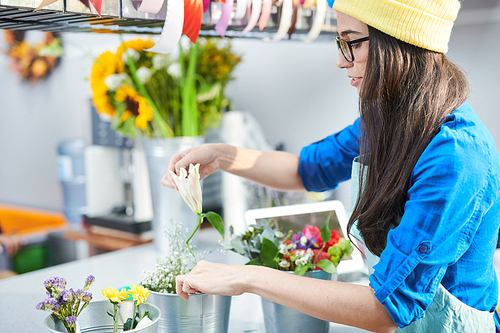 Side view portrait of contemporary young woman lovingly arranging flower compositions while working in shop