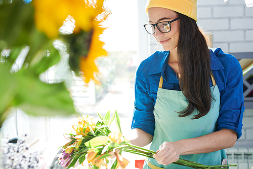 Portrait of modern young woman wearing beanie hat arranging flower compositions and smiling happily while enjoying work in shop, copy space
