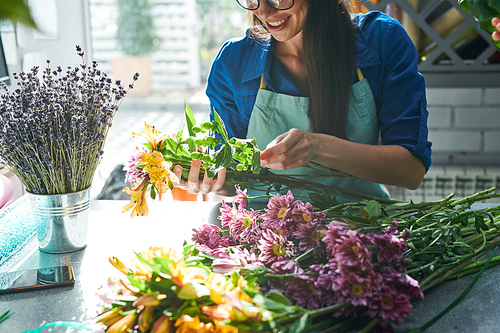 Closeup portrait of modern  female florist arranging fresh flowers while making bouquets in flower shop