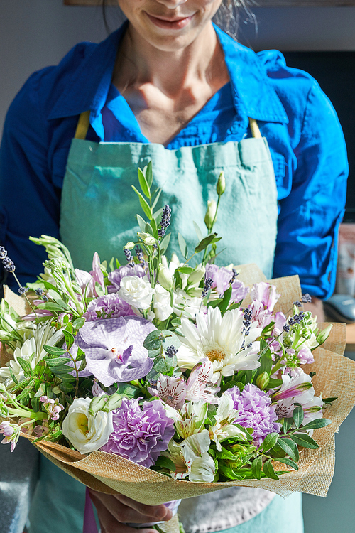Mid section portrait of unrecognizable female florist holding beautiful bouquet lit by sunlight while posing in flower shop
