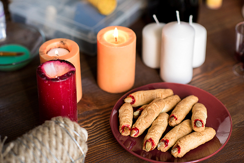 Close-up of creepy witch finger cookies on plate, burning candles on wooden table, Halloween concept
