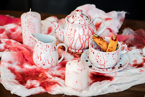 Bloody tea party: close-up of bloody stains in teapot, milk jug, cup and candles on dirty gauze