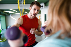 Portrait of  handsome personal trainer motivating young  woman training with dumbbells in gym, copy space