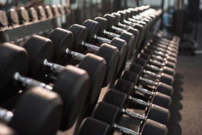 Background image of dumbbells in row on equipment stand in modern gym, copy space
