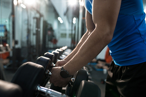 Side view close up of strong male hands picking up dumbbells from equipment stand in modern gym, copy space