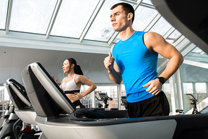 Waist up portrait of two fit young people, man and woman, running on treadmills in modern gym, copy space