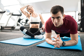 Portrait of  people exercising on mats in health club, focus on strong young man doing plank, copy space