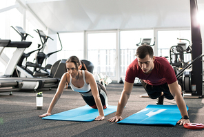 Portrait of young sports couple pushing up on mats in modern gym, copy space