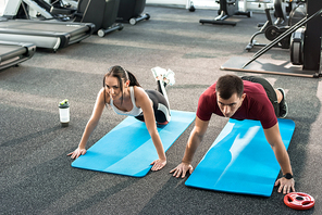 Full length high angle view at young sports couple pushing up on mats in modern gym, copy space