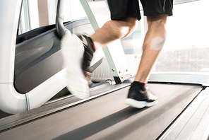 Blurred motion of muscular  male legs running on treadmill lit by sunlight
