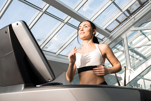 Waist up portrait of fit young woman enjoying running on treadmill in modern gym under glass roof, copy space