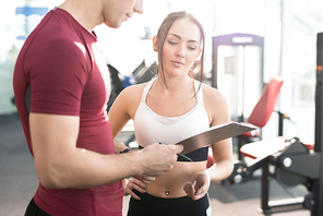 Waist up portrait of young woman signing contract with personal fitness coach in modern gym club
