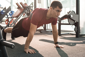 Full length portrait of handsome muscular man doing push ups training in modern gym