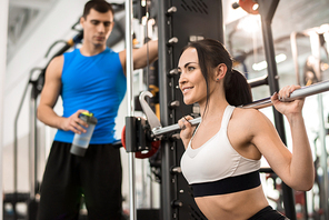 Portrait of beautiful young woman smiling happily while  training with barbell in modern gym, copy space