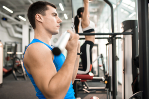 Side view of two people exercising on machines in modern gym by window, focus on handsome muscular man