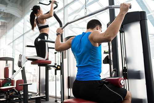 Side view of two people exercising on machines in modern gym by window