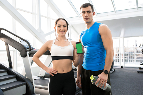 Portrait of fit young couple wearing sports clothes presenting mobile app holding smartphone with green screen and 