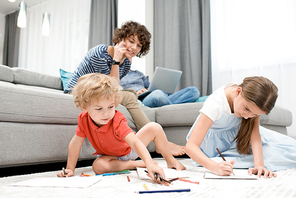 Portrait of two children drawing pictures sitting on carpet in living room with mom watching them from sofa