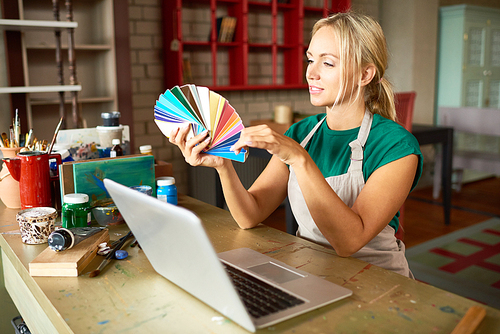 Portrait of blonde female artist looking at color swatches choosing palette for art and craft project in workshop