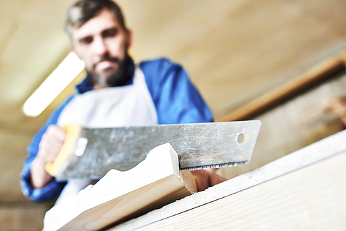 Low angle view of  carpenter sawing piece of wood, focus on foreground