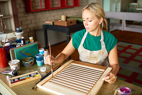Portrait of pretty blonde woman enjoying work in art studio making DIY interior decoration