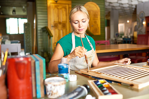 Portrait of pretty blonde woman enjoying work in art studio painting shutters with bronze paint, making DIY interior decoration
