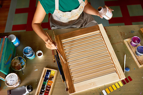Above view of unrecognizable young woman enjoying work in art studio painting shutters with bronze paint, making DIY decoration for interior