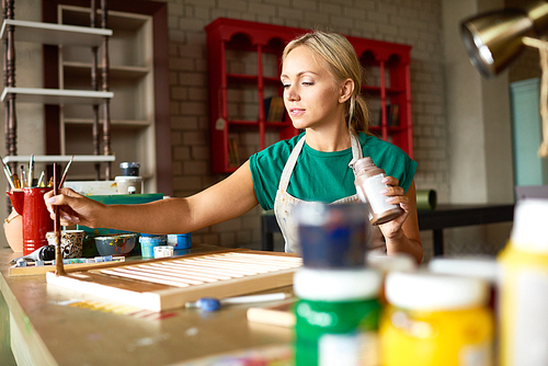 Portrait of pretty blonde woman enjoying work in art studio painting shutters with bronze paint, making DIY interior decoration