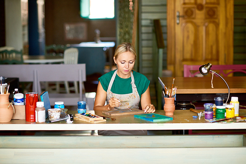 Portrait of pretty blonde woman enjoying work in art studio painting picture on wood making DIY decor, copy space
